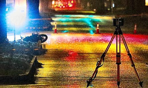 As seen from behind the crime-scene tape two blocks away, the crashed motorcycle lay on the ground while an officers documentation instrument stood on its tripod near the fatal crash, as the heavy rain continued.