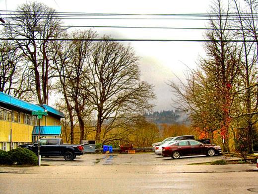 This is the middle of the two-block long property, here looking across Milwaukie Avenue westward on S.E. Harold Street  about where the center of the new high-rise will be. The railing at the back of the parking lot is to keep people from going over the edge and falling into Oaks Bottom.